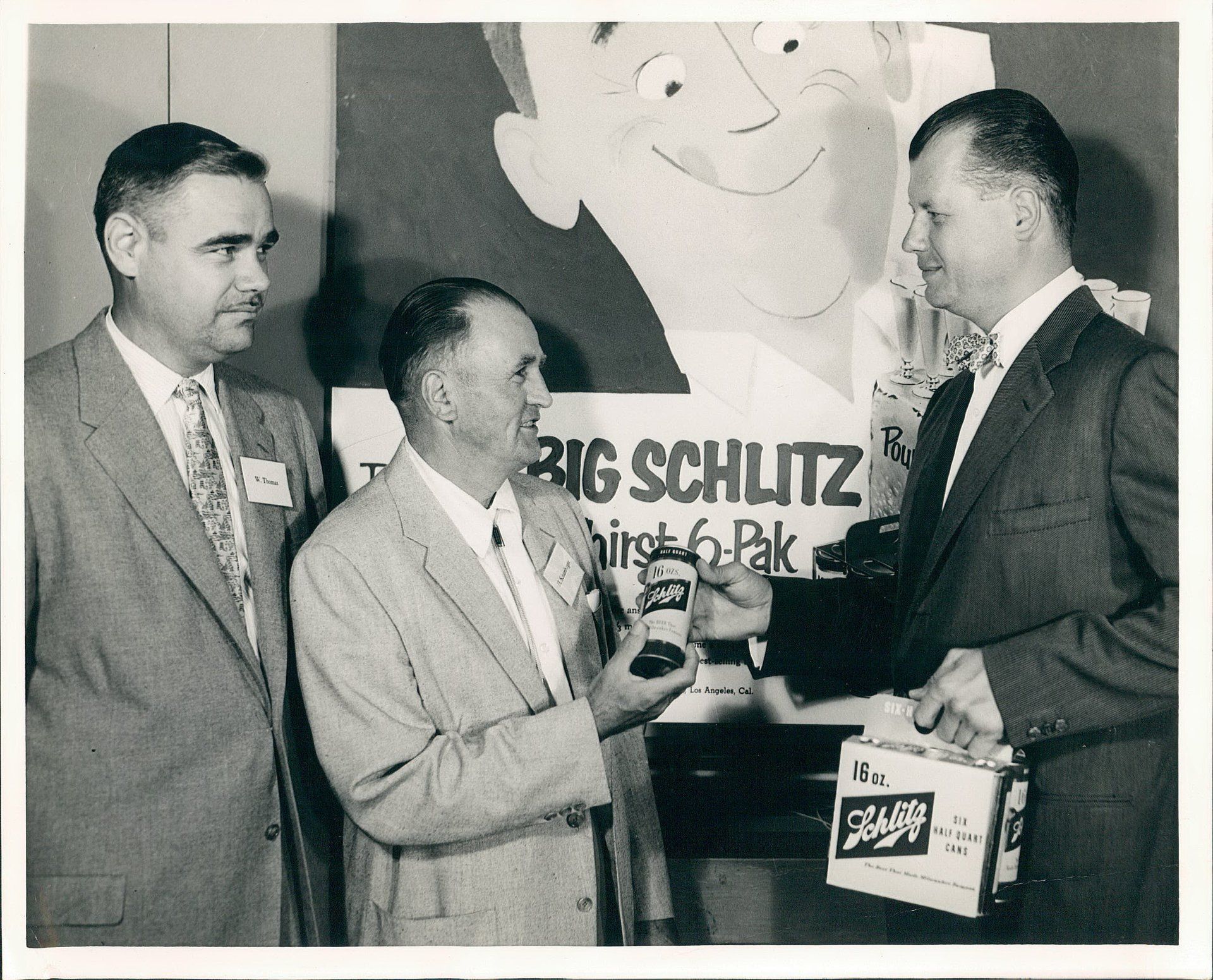 Three men are standing in front of a big schlitz sign