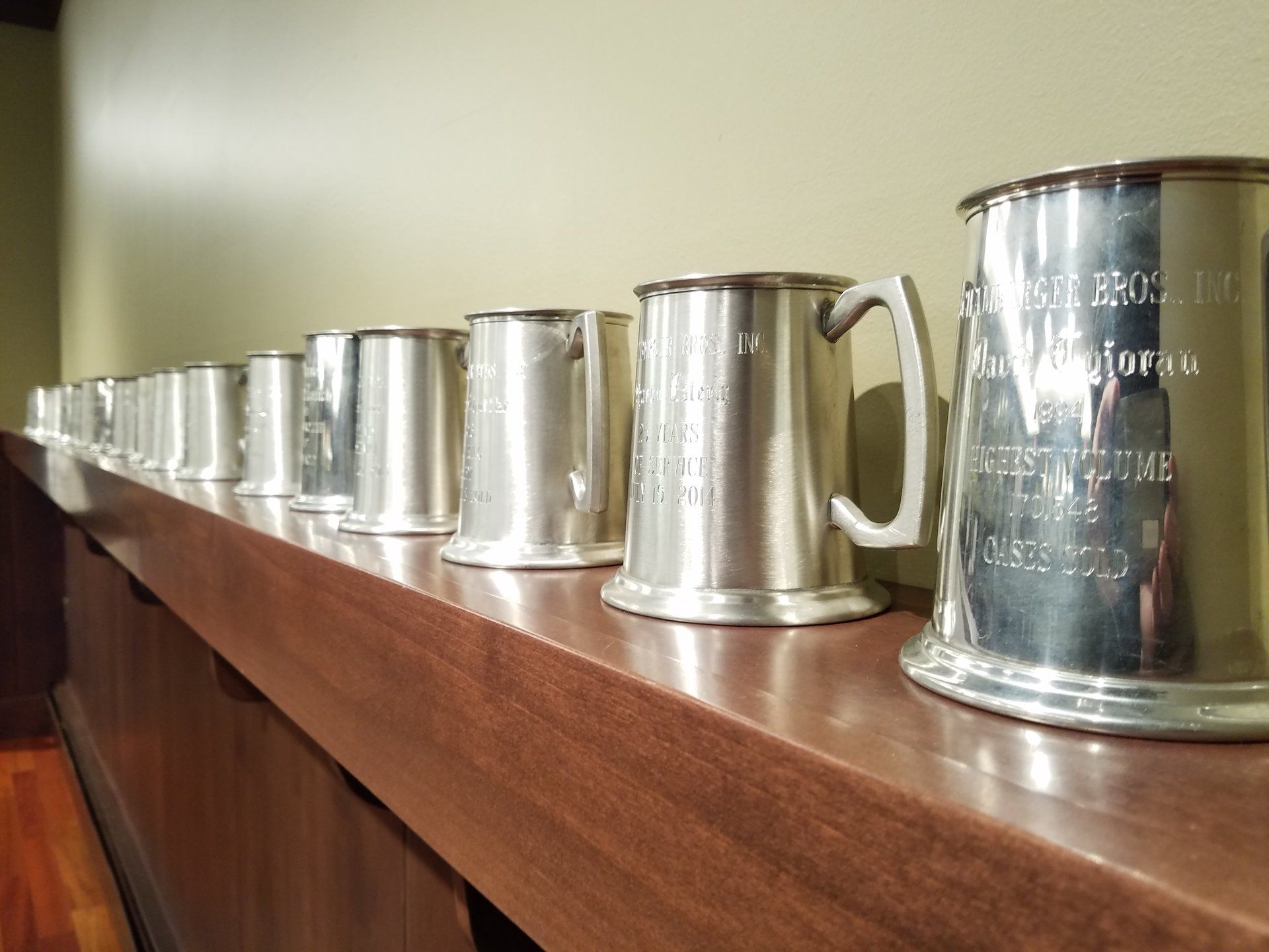 A row of silver mugs are lined up on a wooden shelf