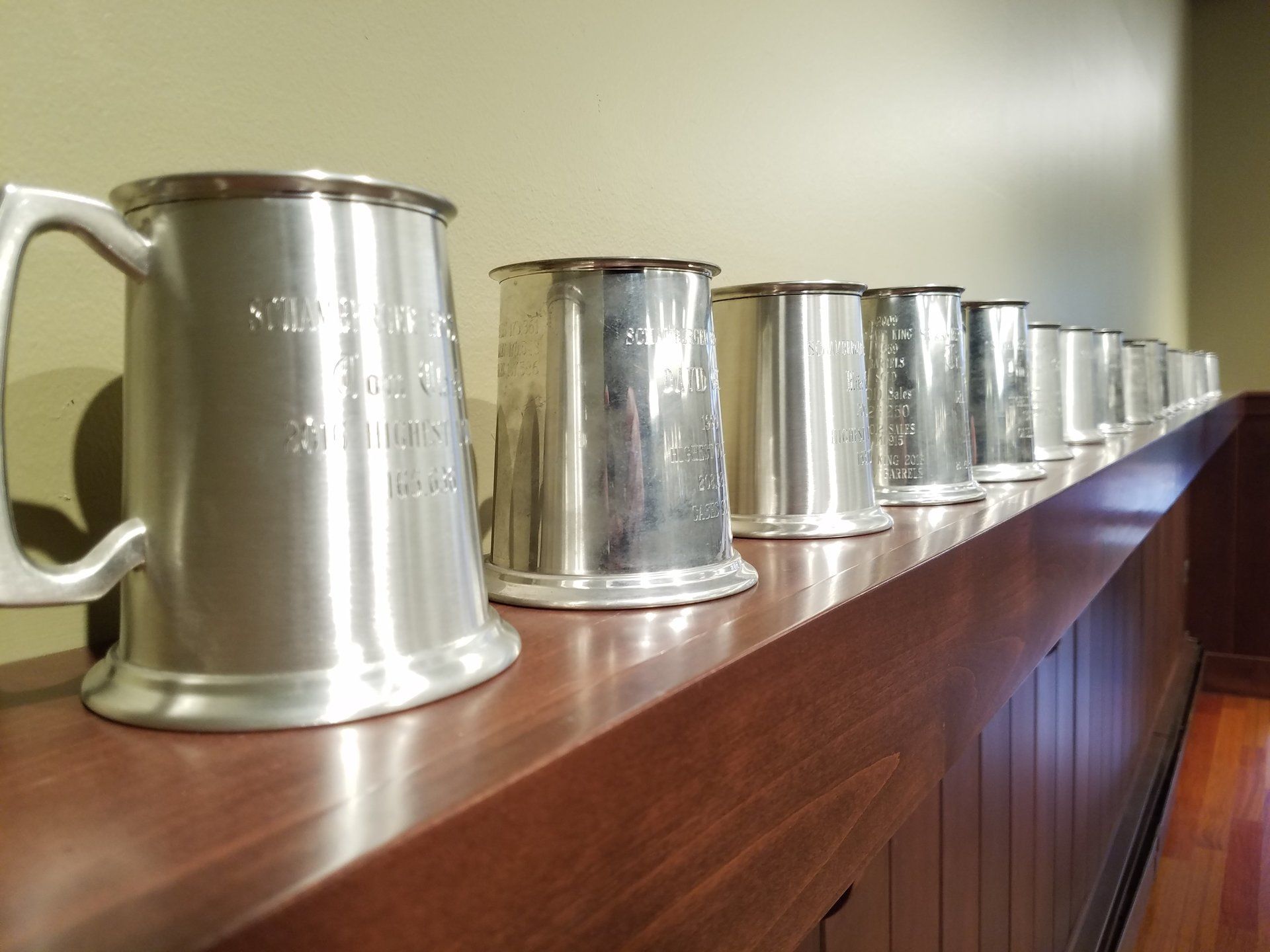 A row of silver mugs are lined up on a wooden shelf