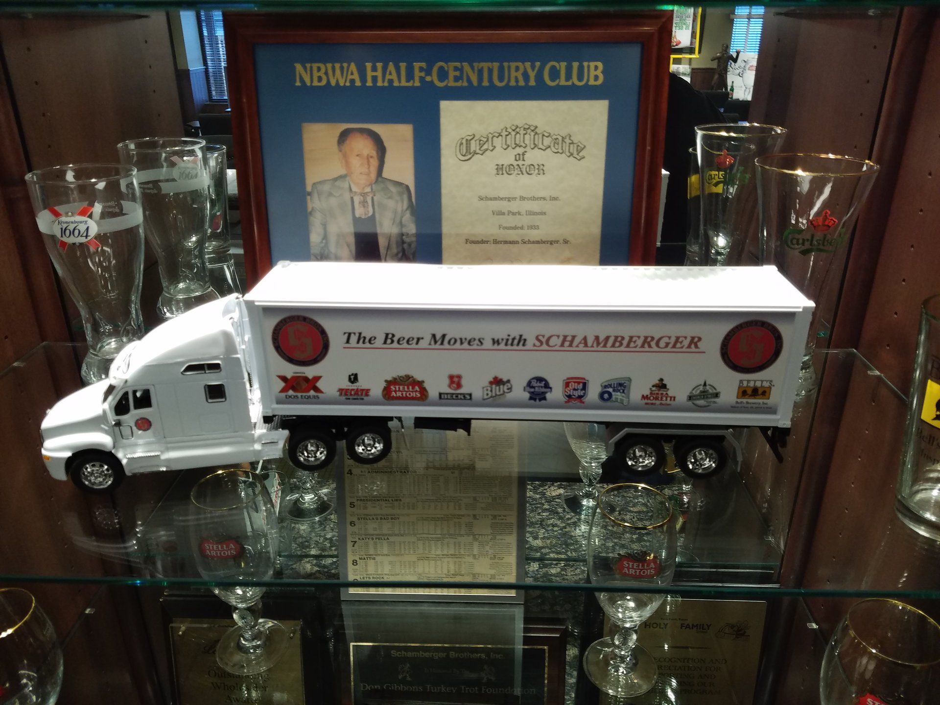 A toy truck is on a glass shelf in front of a new york half century club certificate