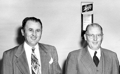 Two men in suits and ties are standing next to each other in a black and white photo.