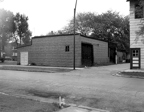 A black and white photo of a brick building on the corner of a street.