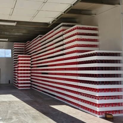 Tall, stacked rows of white foam trays containing rows of small red cylinders, arranged in a warehouse storage area.