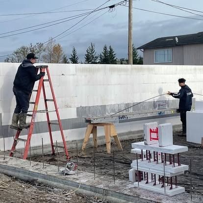 Two workers build a wall using interlocking foam blocks on a construction site.