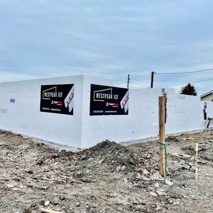 A construction site shows a foundation made of white Westpeak ICF blocks with two company signs on an overcast day.