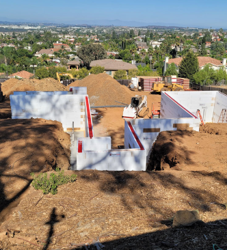 Construction site with white foam block foundation walls installed in trenches on a sunny day.