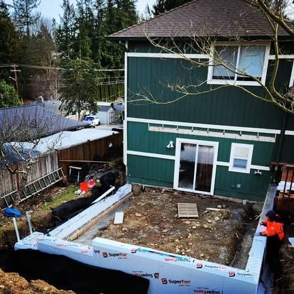 A green house under construction with a newly poured concrete foundation surrounded by white insulation panels.