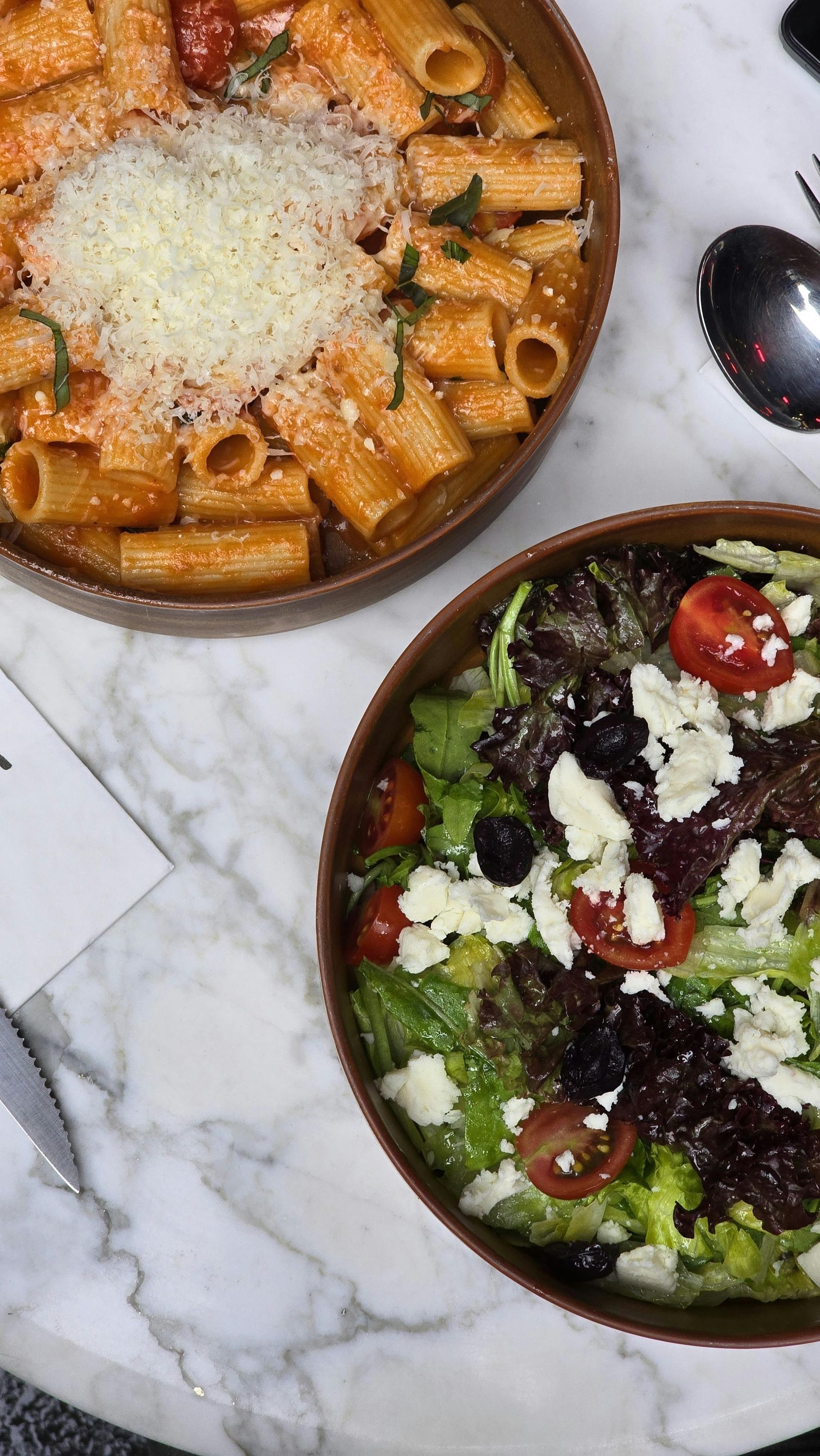 Two bowls of pasta and a salad are on a table.
