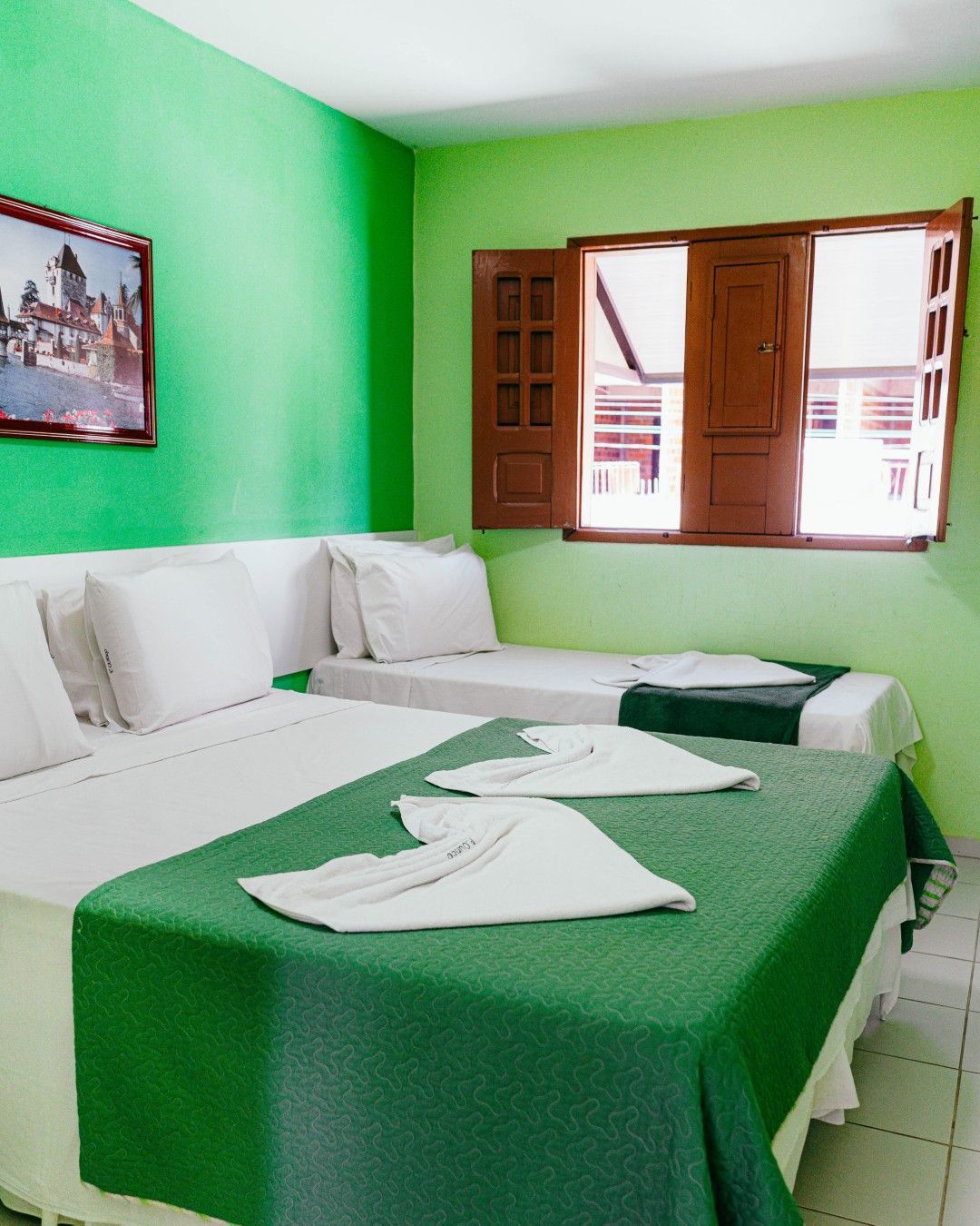 Quarto verde com duas camas e janela aberta.