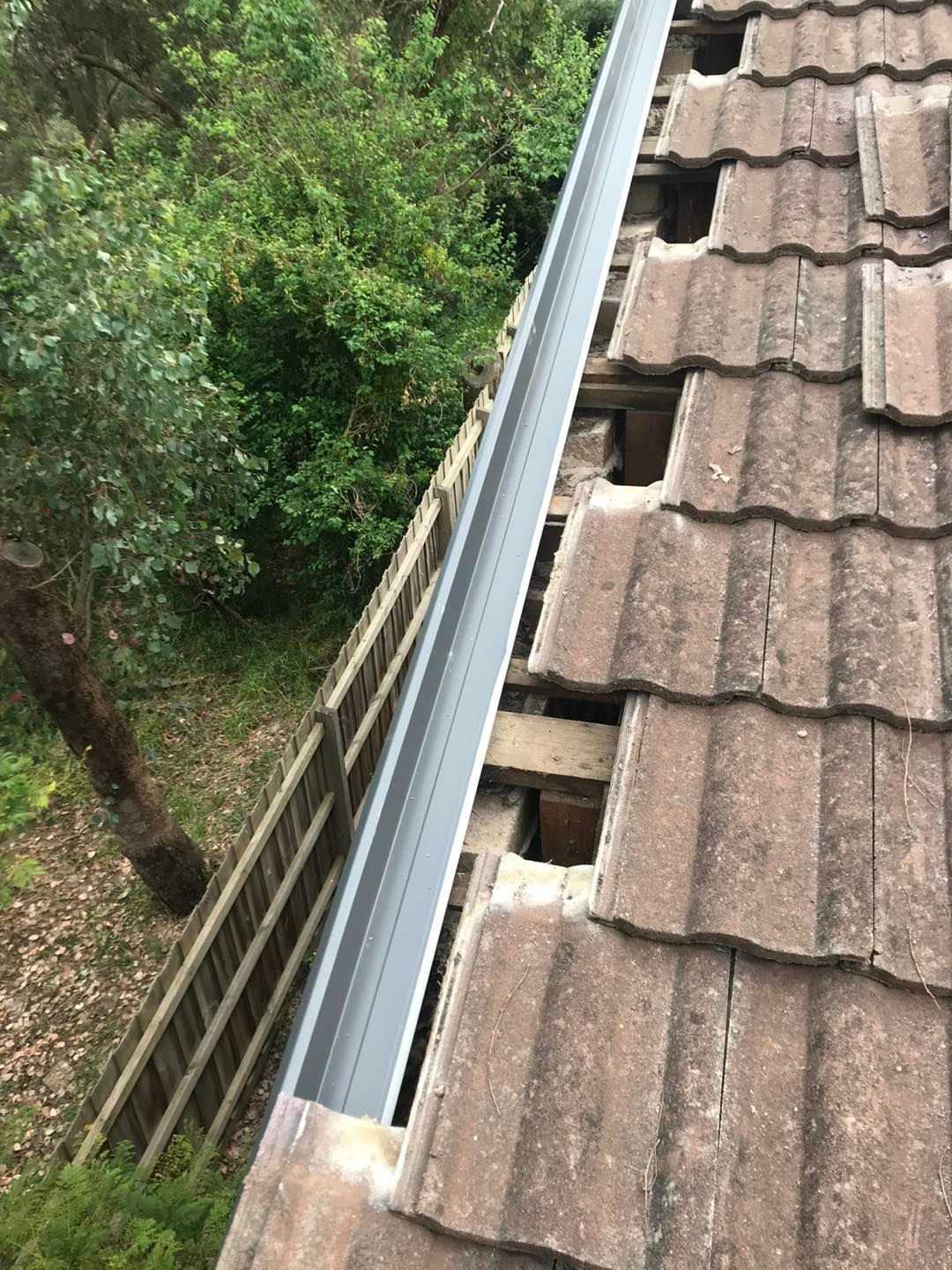 A gutter is sitting on top of a tiled roof next to a wooden fence.