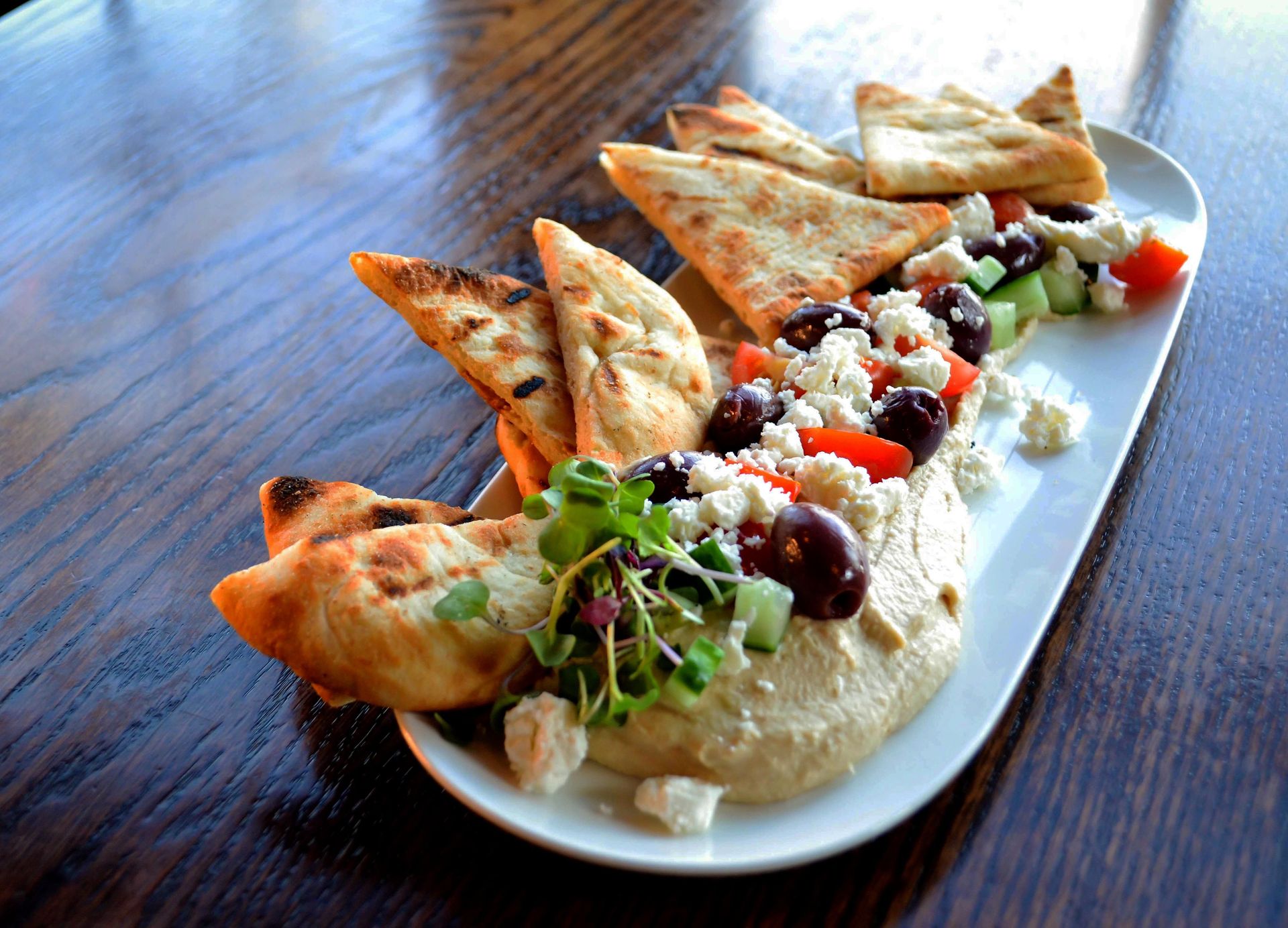 A white plate topped with hummus and pita bread on a wooden table.