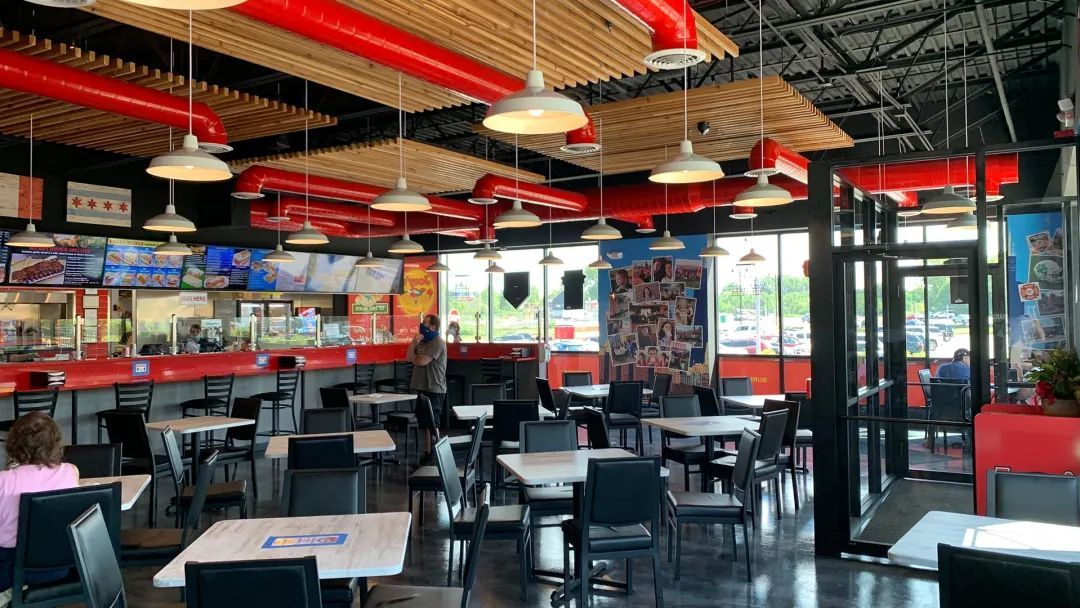 Interior of a brightly lit restaurant with tables and chairs. Red accents, TVs on the wall, and ductwork on the ceiling.