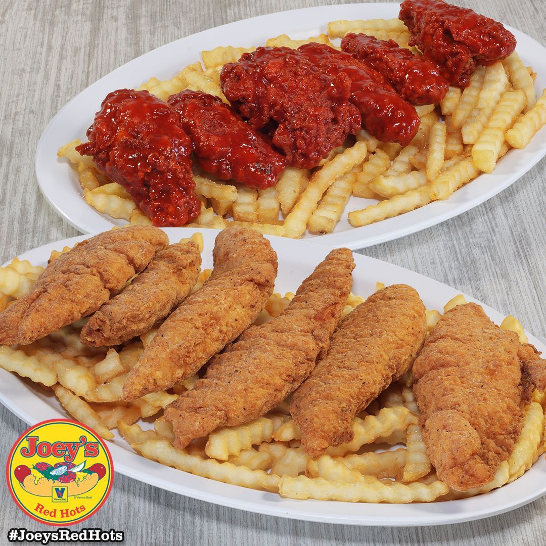 Plates of fried chicken wings and tenders with french fries. Red and brown food on white plates.