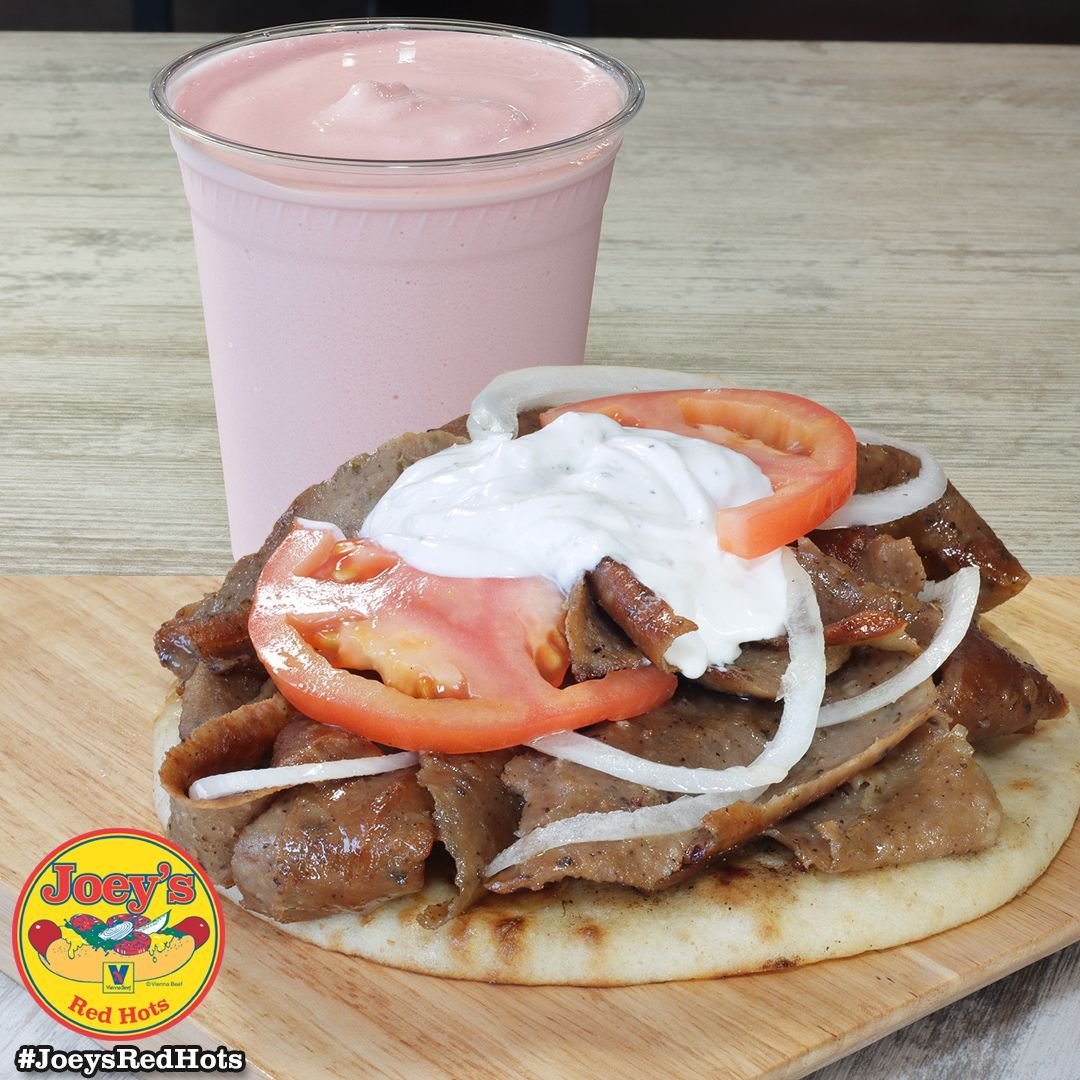 Gyro sandwich with tzatziki, tomato, and onion next to a pink milkshake.