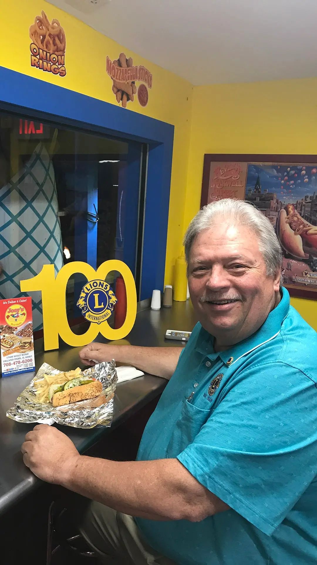 Man smiling at counter with foil-wrapped food, near a 