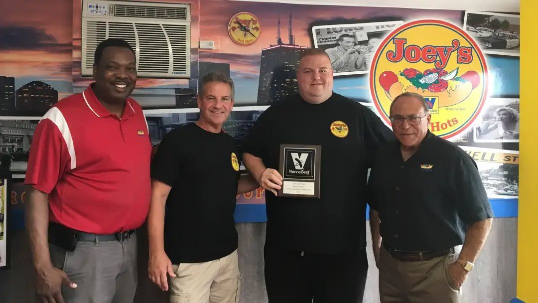 Four men standing, holding an award in front of a colorful wall at Joey's Pizza restaurant.