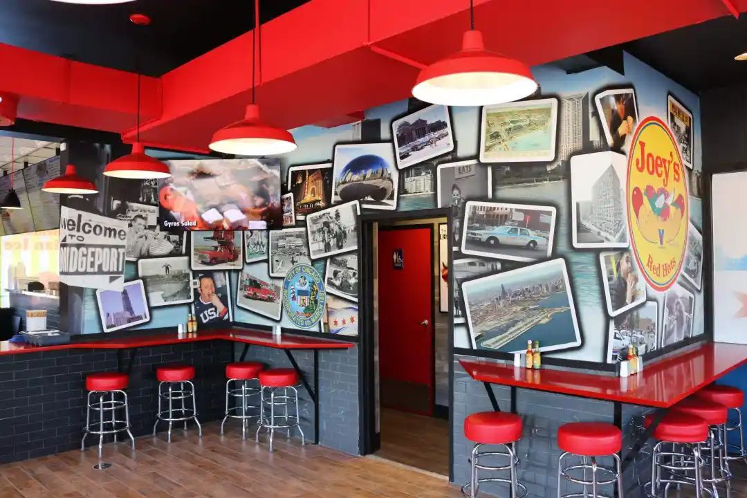 Interior of a diner with red accents, stools, and wall art featuring photographs; bright overhead lighting.