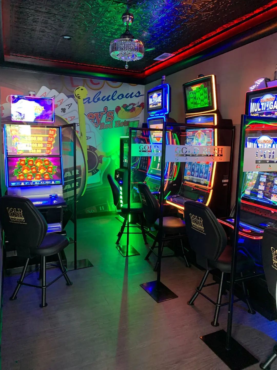 A casino slot machine area. Several machines with bright screens and chairs are visible. Green and blue lighting.