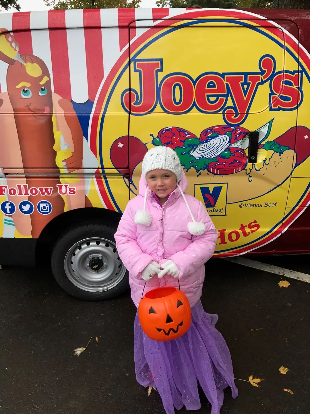 Girl in mermaid costume, holding pumpkin bucket, in front of Joey's Hot Dogs food truck.