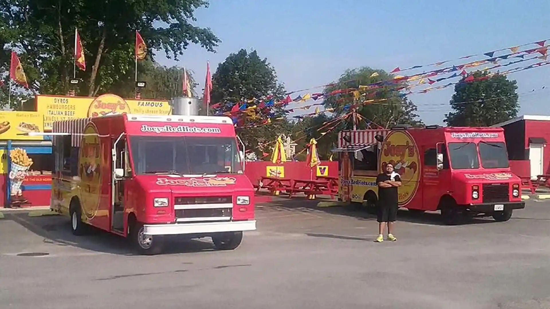 Red and yellow food trucks parked outdoors with colorful flags and a person standing nearby.