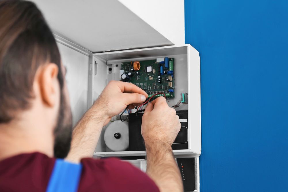 A Man is Fixing a Security System With a Screwdriver — AES Electrical Contracting In Winnellie, NT