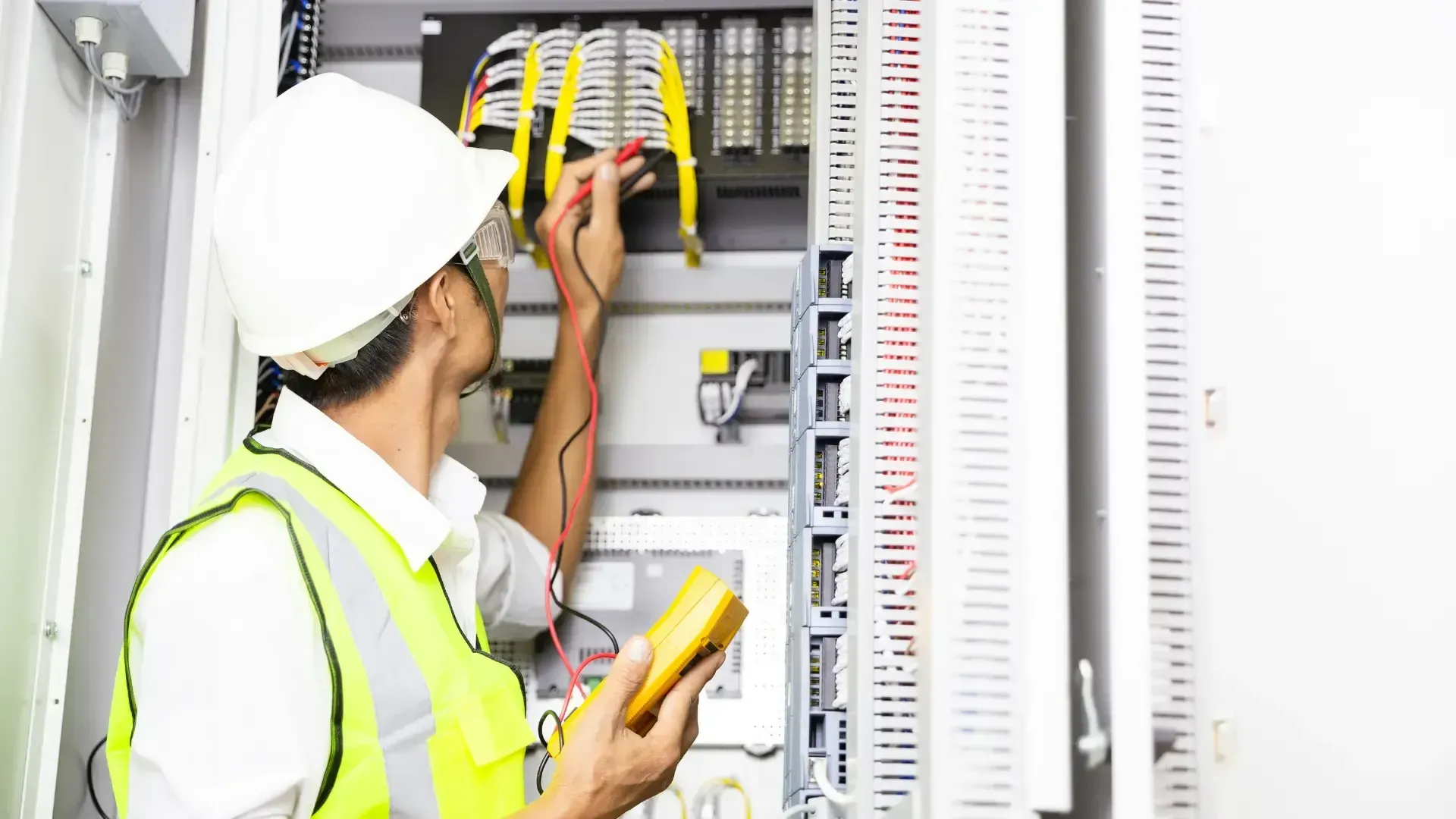 An electrician is working on an electrical box while holding a multimeter.