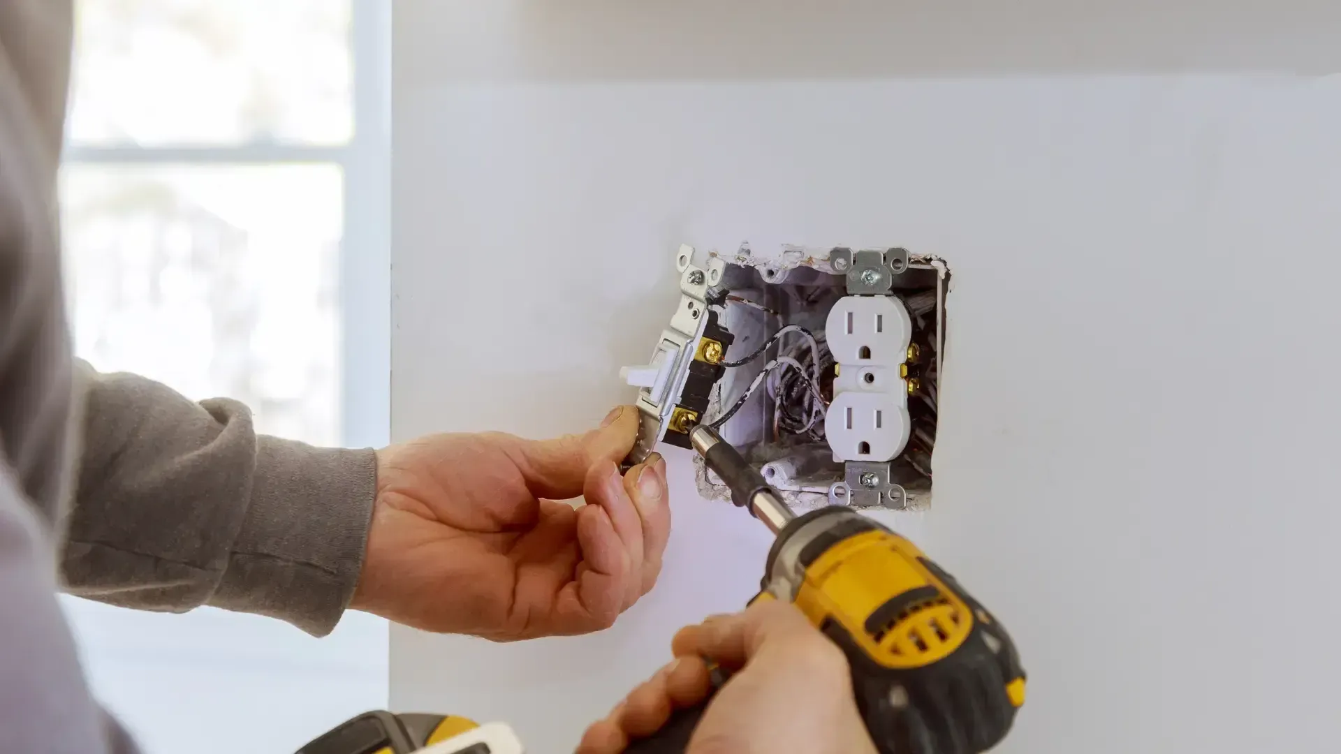 A man is installing an electrical outlet on a wall with a drill.