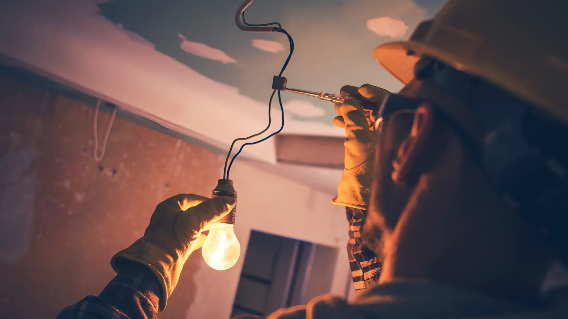 A man is holding a light bulb in his hand while working on a ceiling.