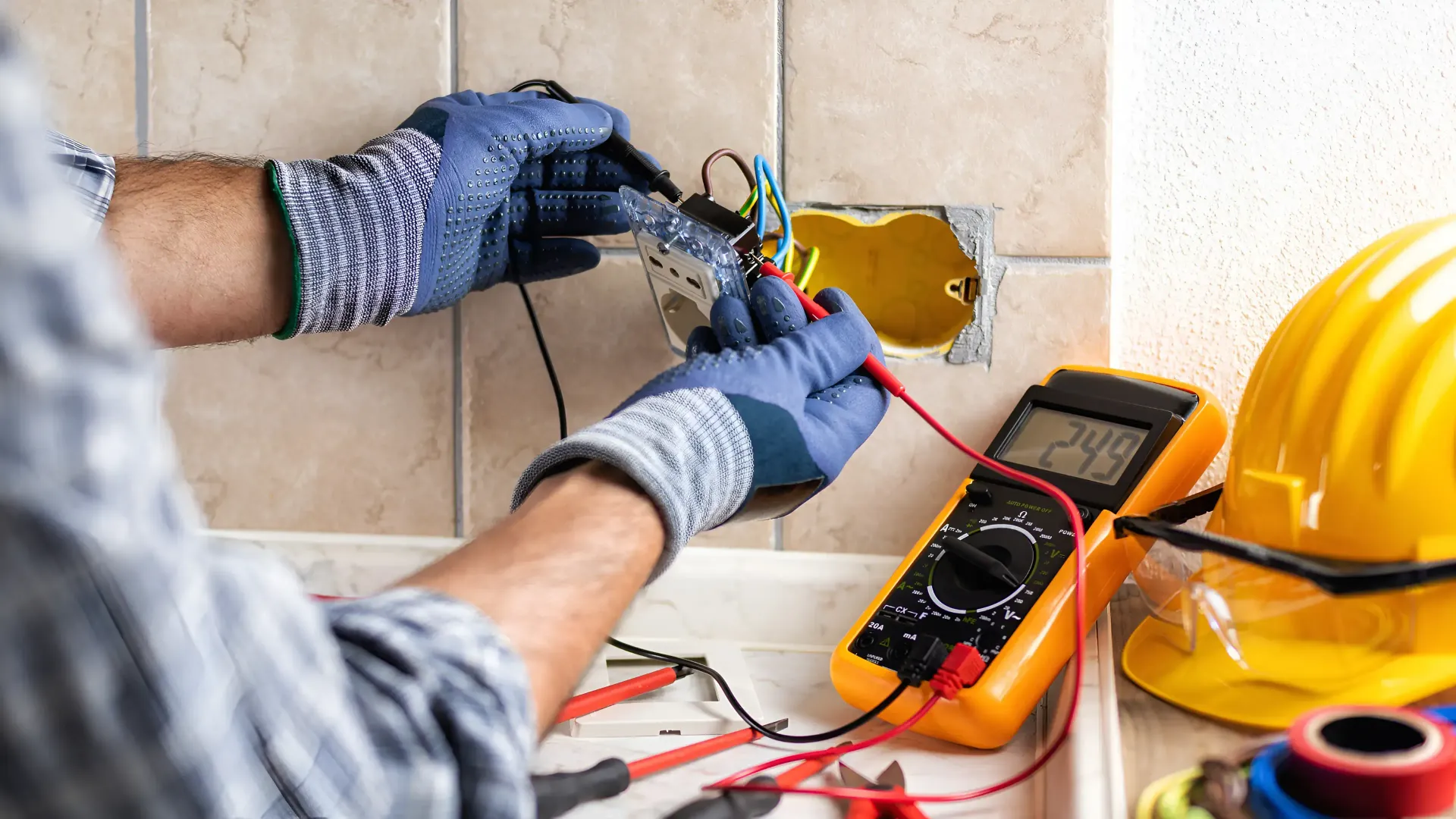 An electrician is working on an electrical outlet with a multimeter.