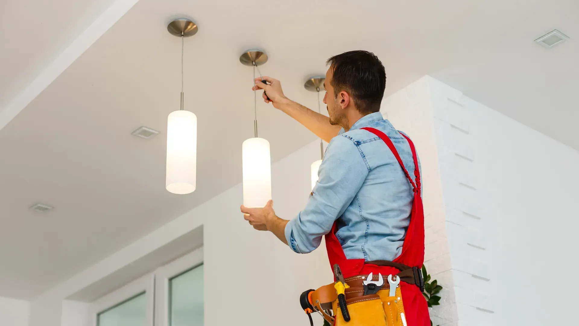 A man is installing a light fixture on the ceiling.