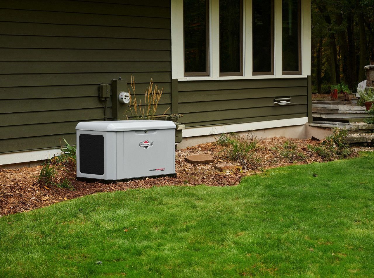 A generator is sitting in the grass in front of a house.