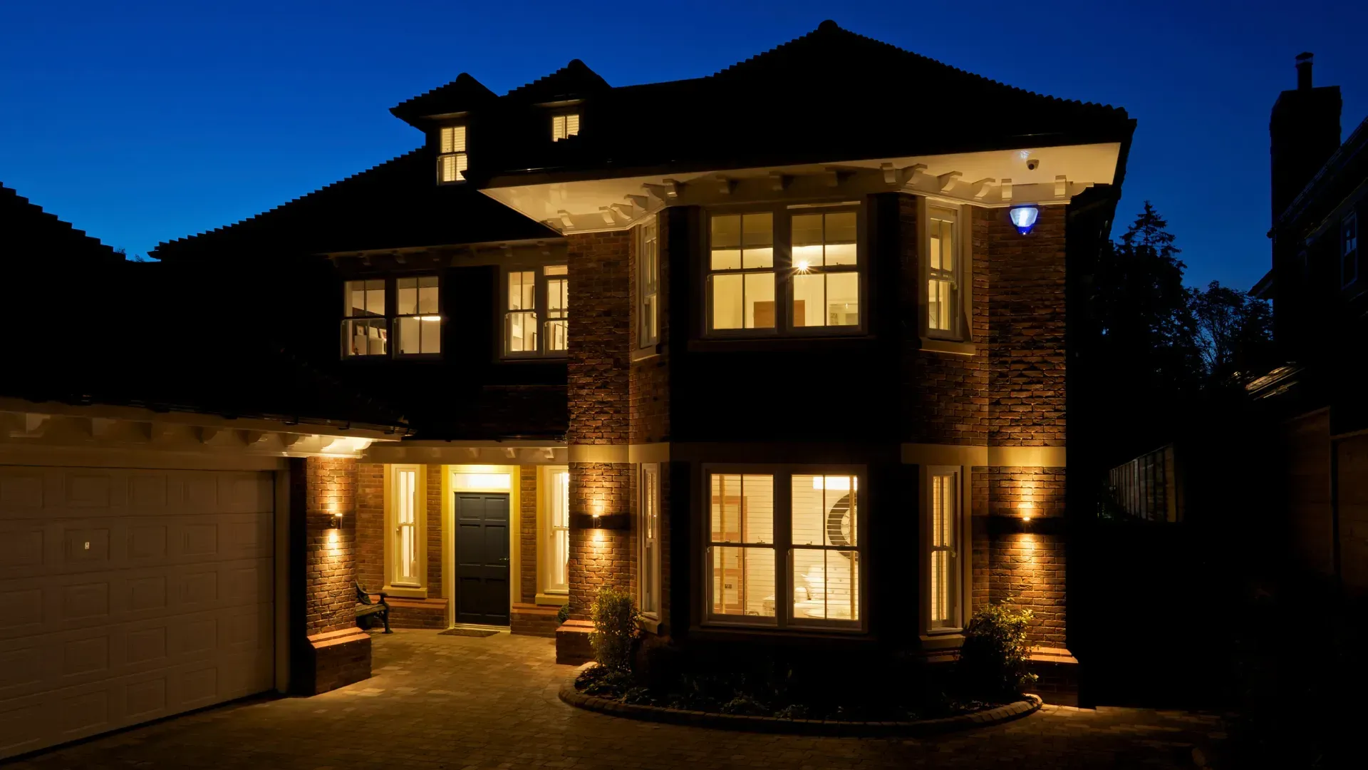 The house is lit up at night and has a garage in front of it.