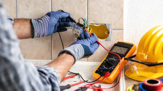 An electrician is working on an electrical outlet with a multimeter.