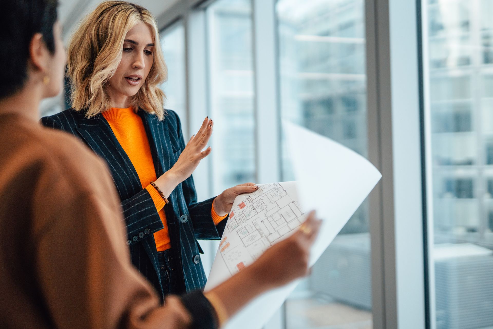 Two people reviewing architectural plans in a modern office. Two people reviewing architectural plans in a modern office.