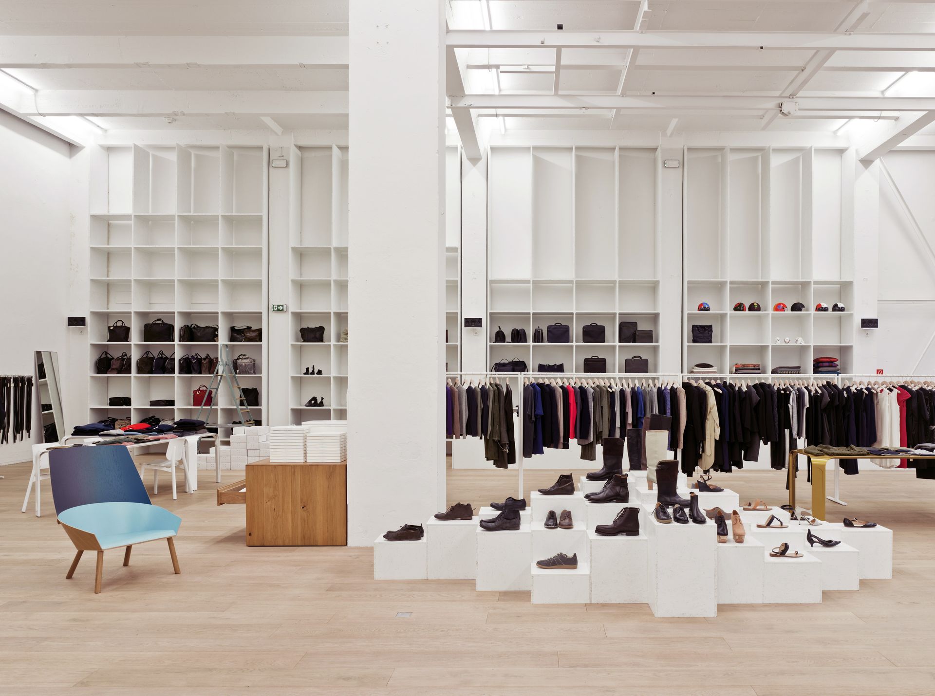 Fashion store interior design with white walls, clothes, bags and shoes on top of boxes.