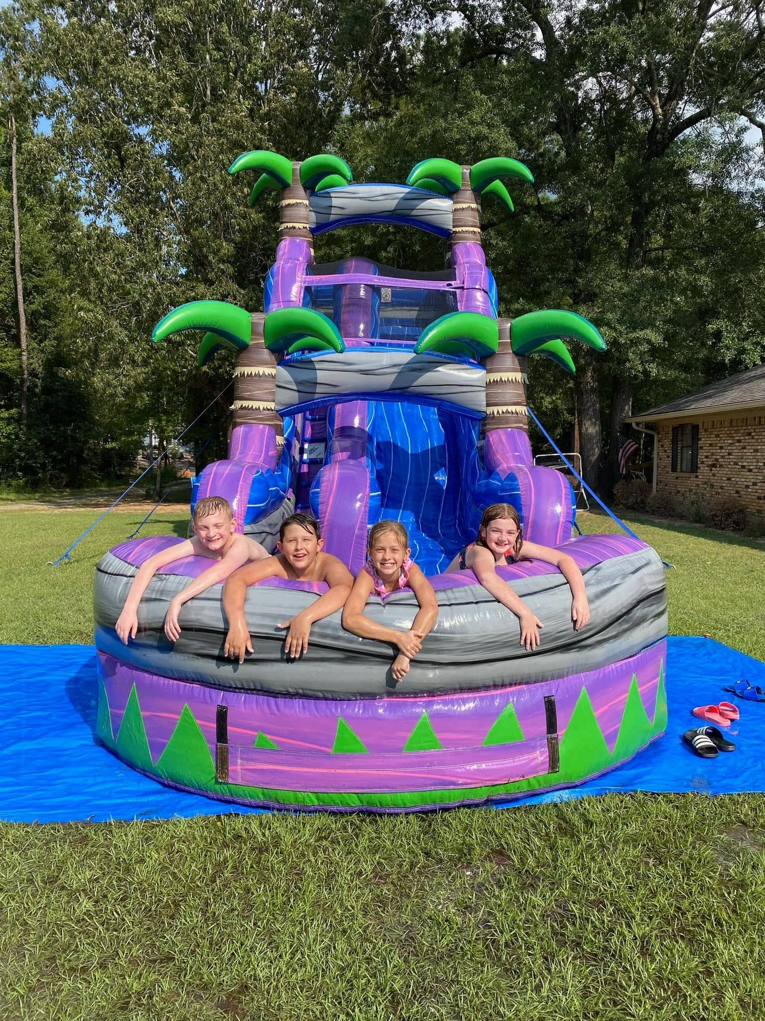Four children on a colorful tropical-themed inflatable bounce house in a grassy yard