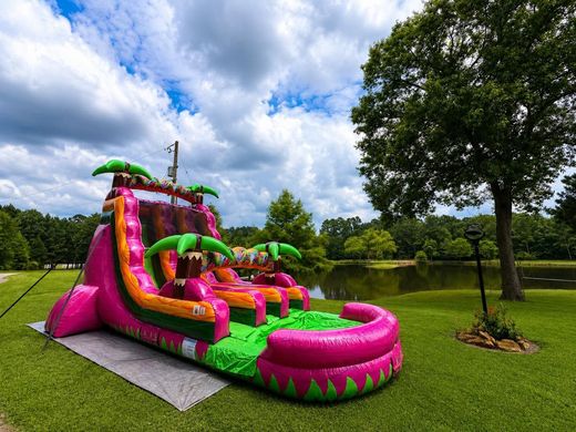 Bright pink and green inflatable waterslide in a grassy park under a cloudy sky