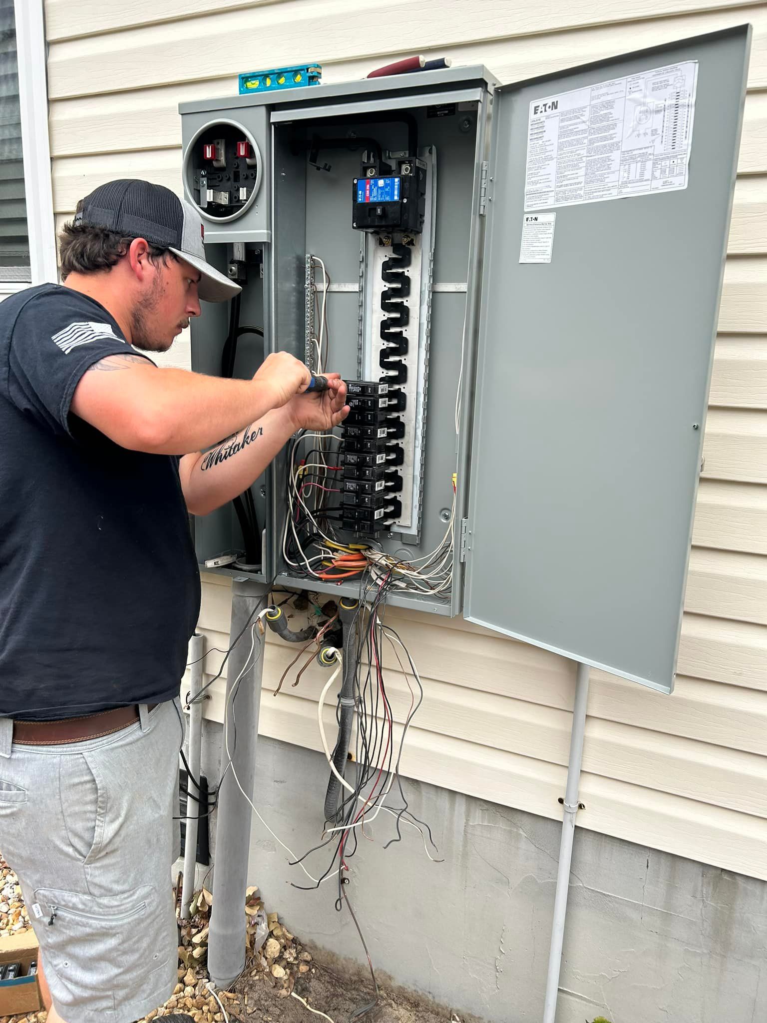 Electrician works on an electrical panel on a building exterior. Wires hang.
