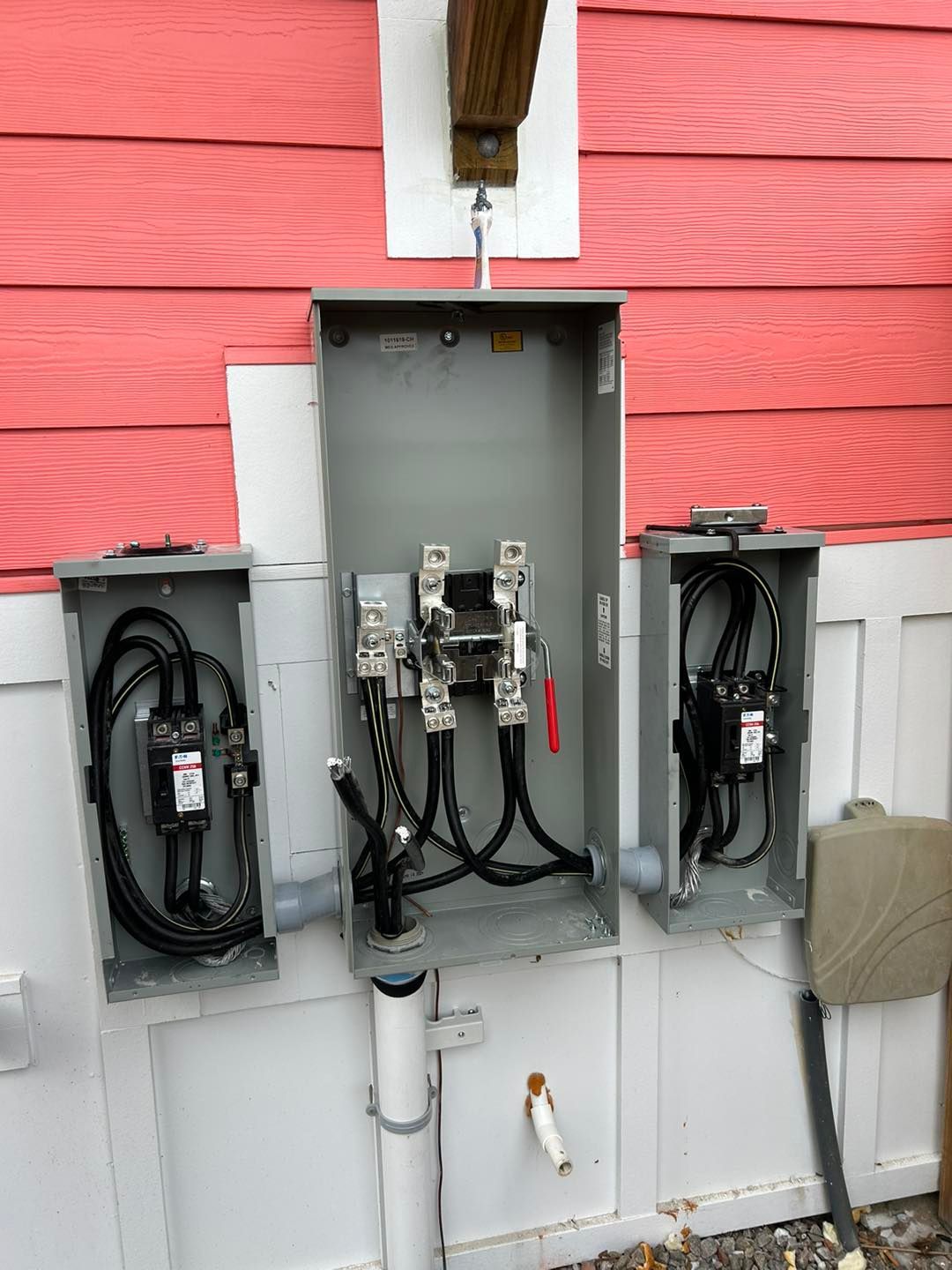Electrical meter boxes on a pink and white exterior wall, containing wiring and switches.