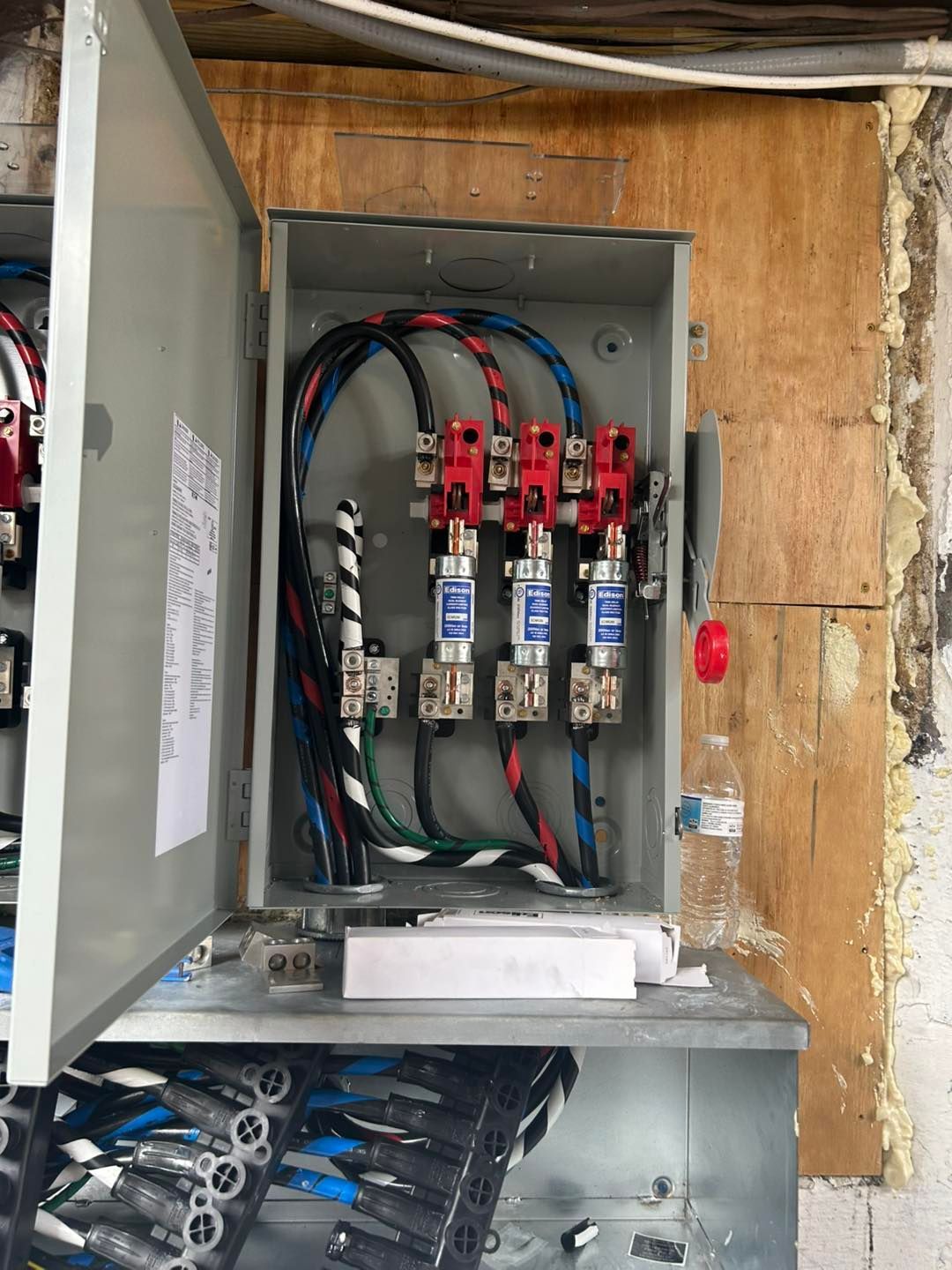 Open electrical box with fuses, wires, and red disconnect lever.