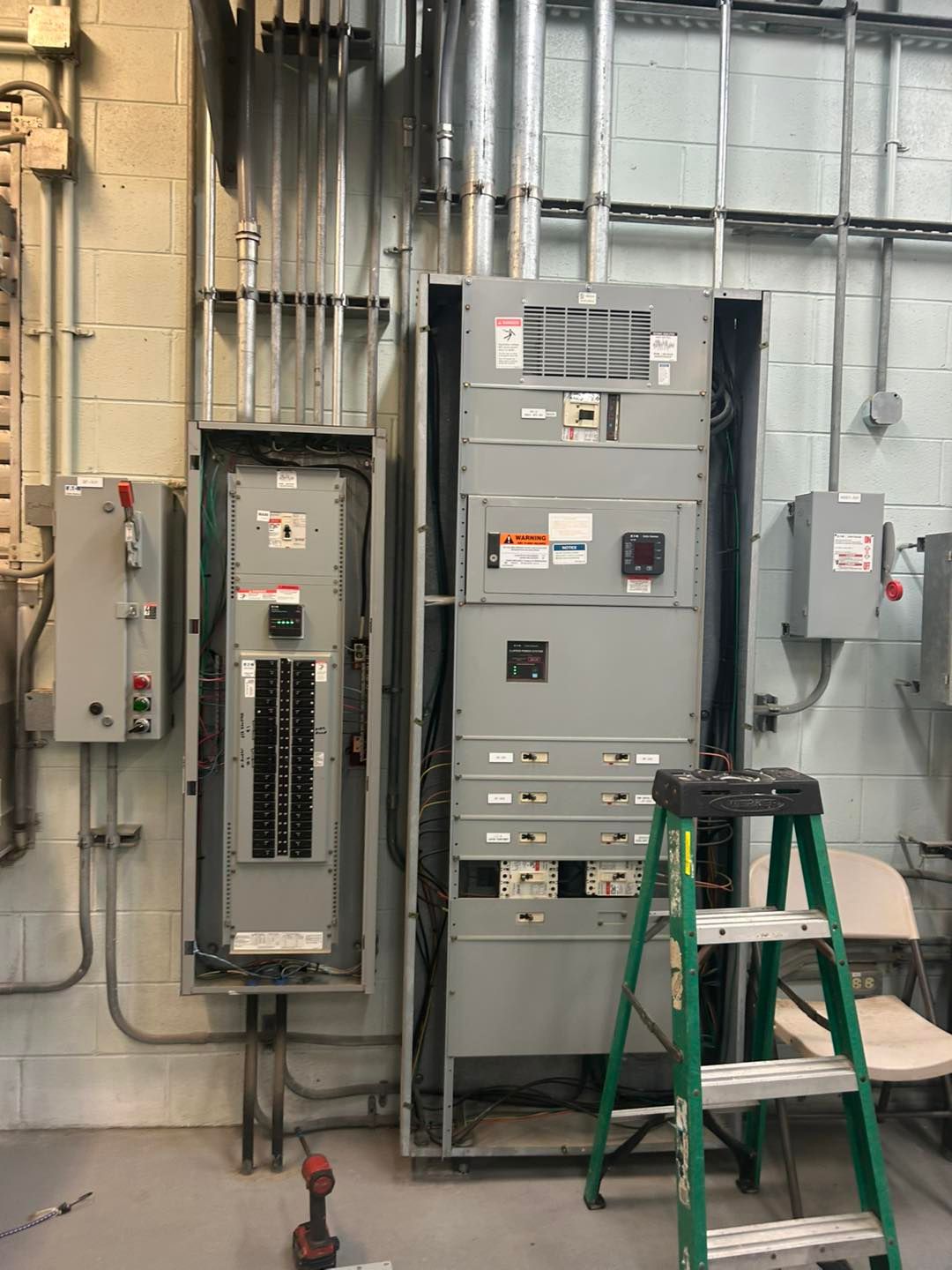 Electrical panel and circuit breaker boxes mounted on a wall, with a ladder nearby.