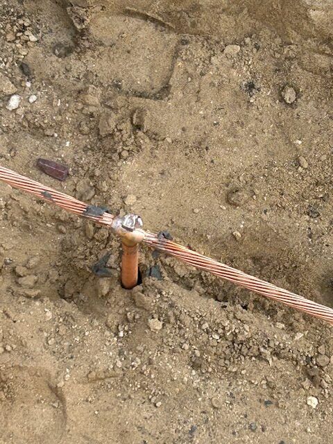 Copper wire and grounding rod connection buried in dirt.