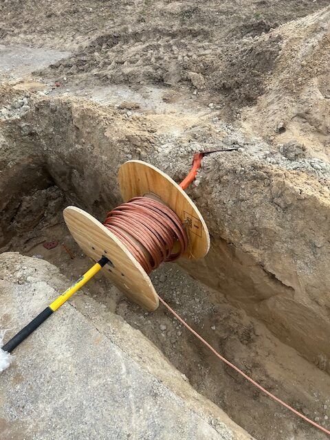 Spool of copper wire in a trench, yellow handle, orange cable at top, construction setting.