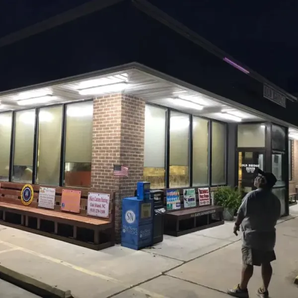 Exterior of a building at night with a person looking up. Benches, windows, and a brick column are visible.