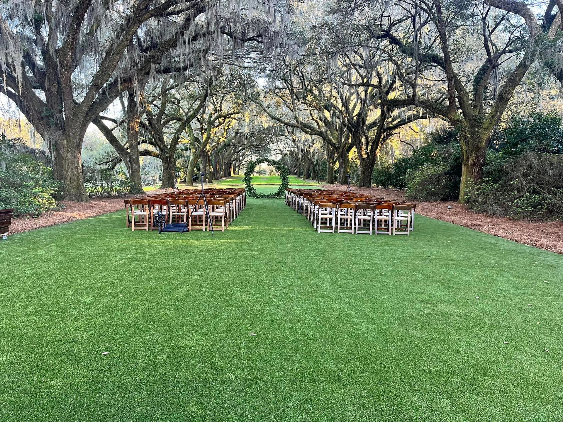a row of chairs are lined up in a lush green field surrounded by trees .