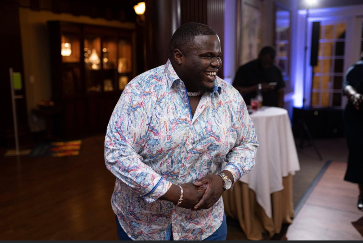 a man in a floral shirt is standing in a room with his hands on his hips .