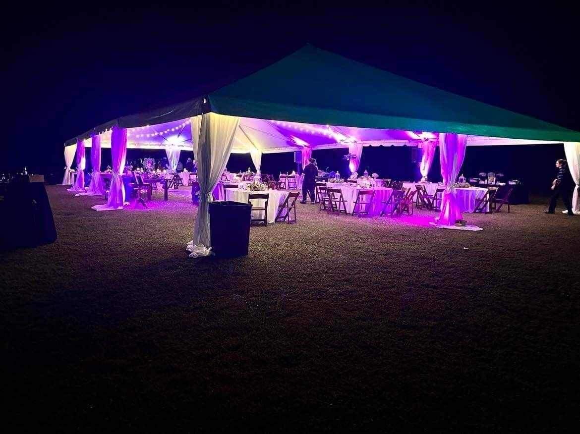 a large tent with tables and chairs underneath it is lit up at night .