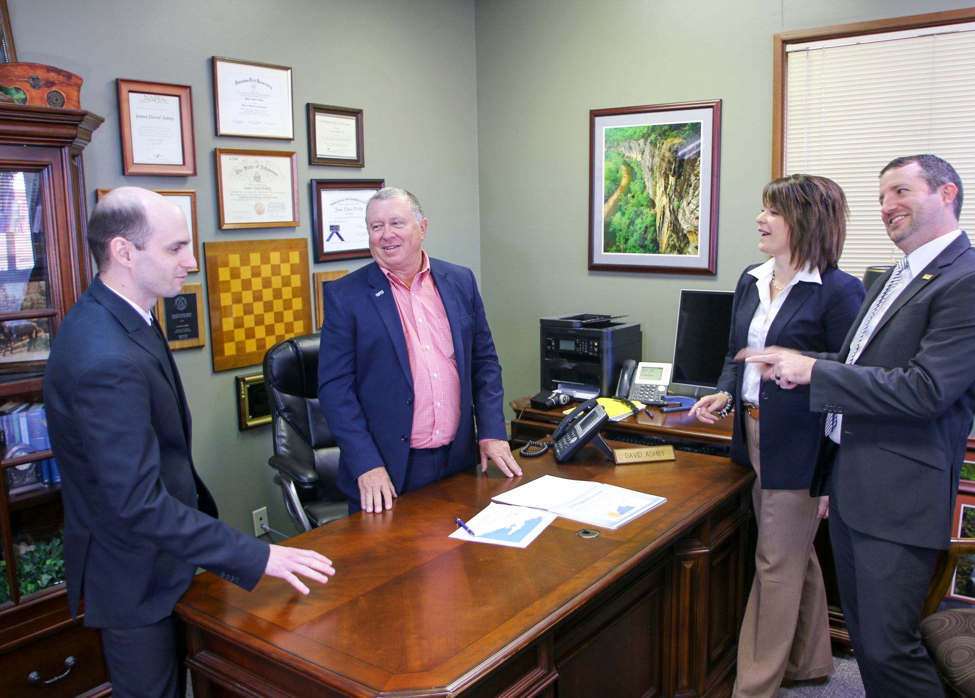 A group of people are standing around a desk in an office.
