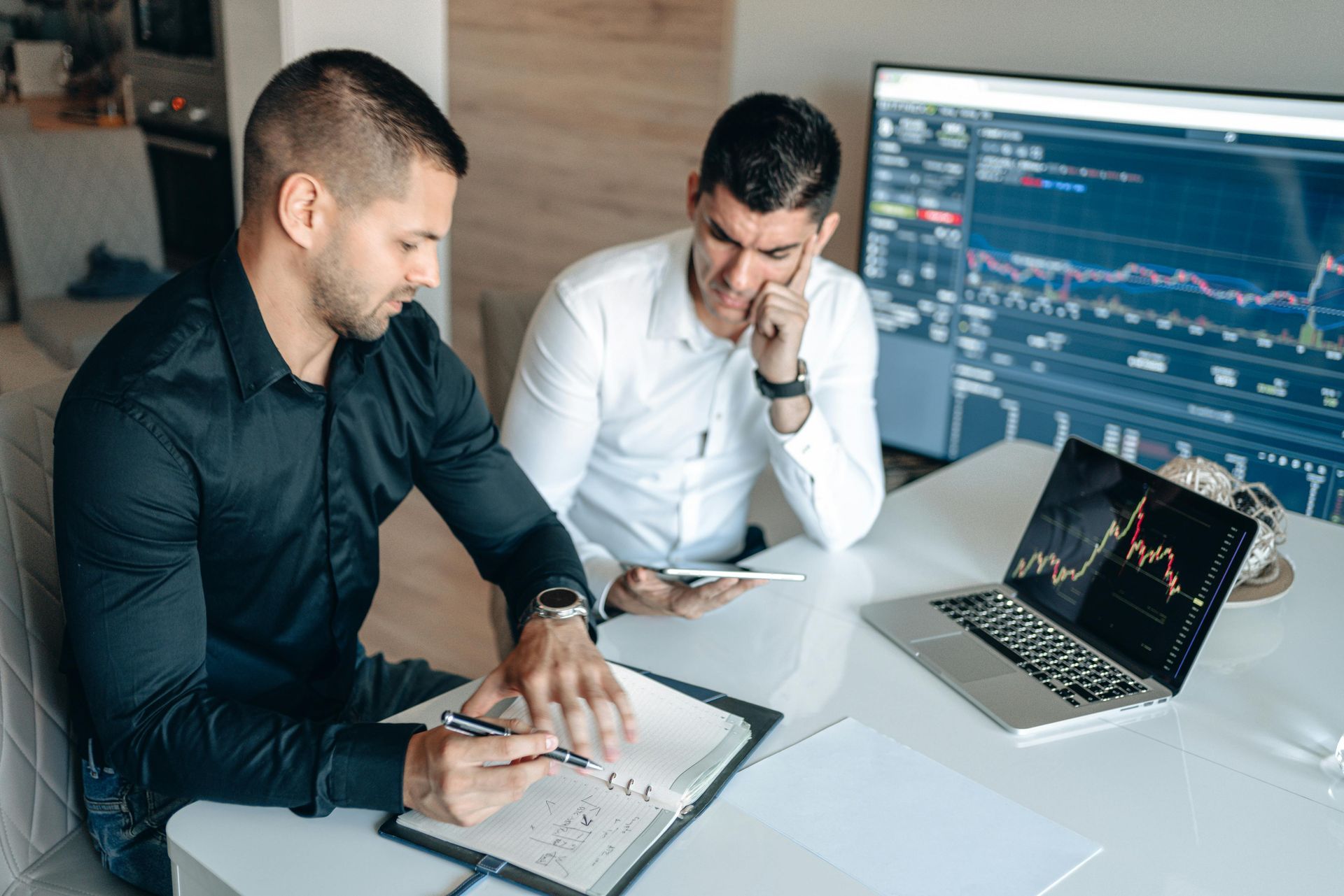 Two men are sitting at a table with a laptop and a tablet.