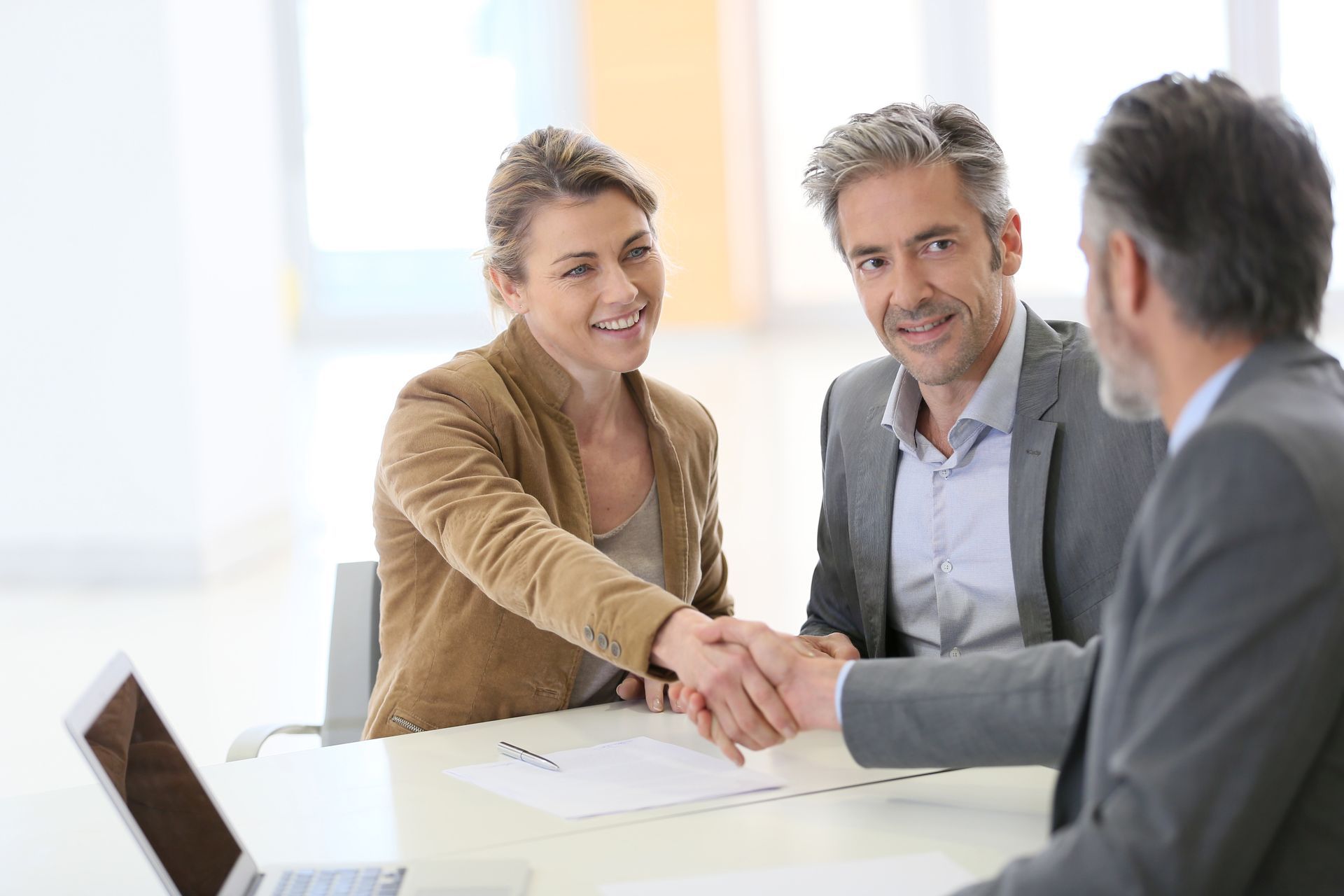 A man and a woman are shaking hands while sitting at a table.